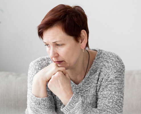 Eine traurige ältere Dame mit Kurzhaarfrisur sitzt auf einer Couch – vitaL